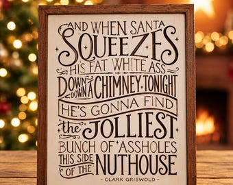 May include: A rectangular wooden sign with a dark brown frame and a light-colored background. The sign features black text that reads: AND WHEN SANTA SQUEEZES HIS FAT WHITE ASS DOWN A CHIMNEY TONIGHT HE'S GONNA FIND THE JOLLIEST BUNCH OF ASSHOLES THIS SIDE OF THE NUTHOUSE - CLARK GRISWOLD -