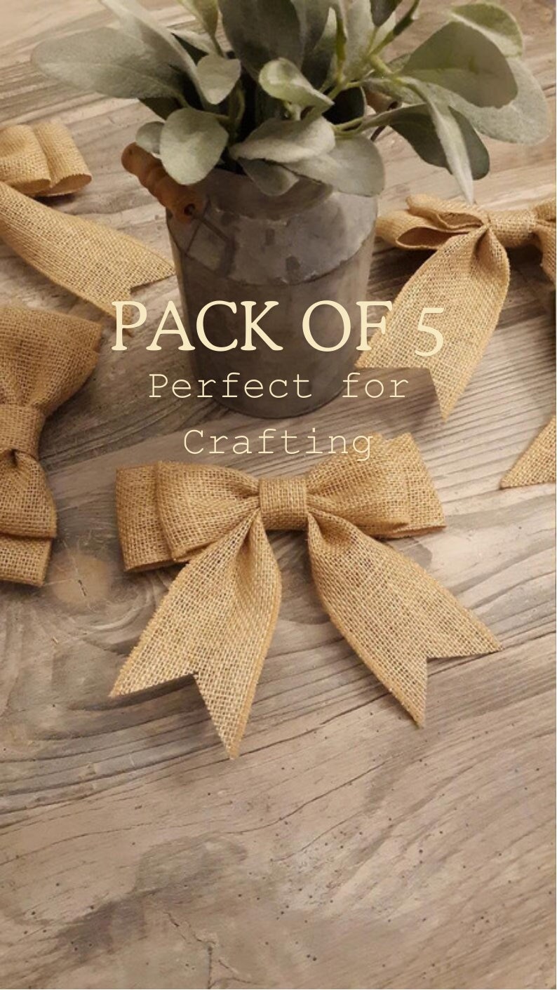 May include: A pack of five tan burlap bows with a woven texture and pointed ends. The bows are arranged around a gray metal container holding green foliage. The text PACK OF 5 Perfect for Crafting is printed in white over the center.