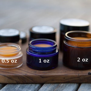 K&ouml;nnte beinhalten: Drei Glasbeh&auml;lter in verschiedenen Gr&ouml;&szlig;en und Farben, die eine gelbe Substanz enthalten. Die Beh&auml;lter sind mit 0,5 oz, 1 oz und 2 oz beschriftet. Die Beh&auml;lter stehen auf einer Holzoberfl&auml;che.