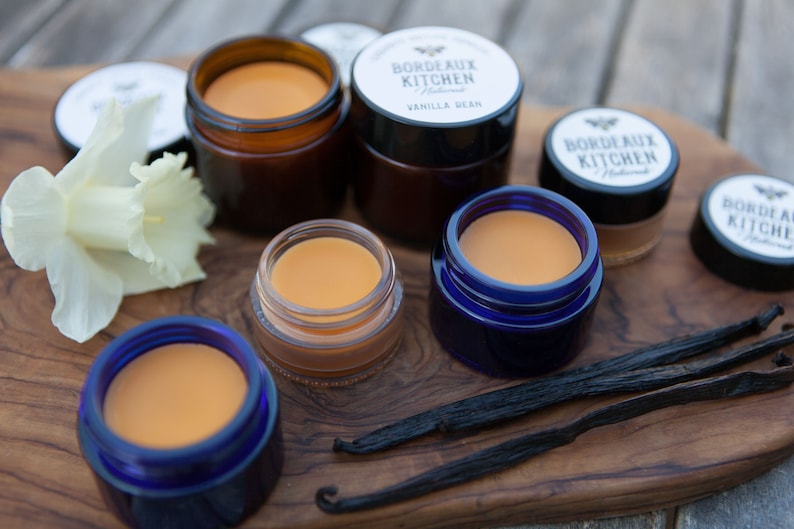 K&ouml;nnte beinhalten: Ein Holzbrett mit f&uuml;nf kleinen Gl&auml;sern Lippenbalsam. Die Gl&auml;ser sind in verschiedenen Farben, darunter blau, braun und klar. Der Lippenbalsam ist hellorange. Auf dem Brett liegen auch zwei Vanilleschoten. Der Text auf den Gl&auml;sern lautet "Bordeaux Kitchen Natural" und "Vanilla Bean".