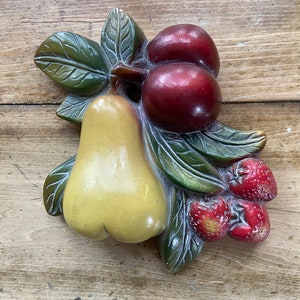 May include: A ceramic wall decoration featuring a yellow pear, red cherries, and red strawberries with green leaves.