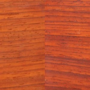 May include: Close-up of Padauk wood grain. The wood has a reddish-orange hue with dark, linear grain patterns. The word "Padauk" is printed in the lower left corner. This image showcases the natural beauty and texture of the wood.