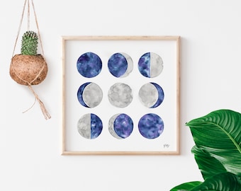 May include: A framed watercolor painting of a moon phases design. The moon phases are depicted in shades of gray and blue, with a starry sky effect in some of the phases.