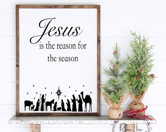 Könnte beinhalten: Ein weißes Schild mit einem Holzrahmen, auf dem der Text "Jesus is the reason for the season" in schwarzer Kursivschrift steht. Unter dem Text befindet sich eine schwarze Silhouette der Weihnachtsgeschichte mit einem Stern darüber.