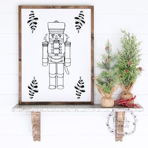 May include: Black and white printable design of a nutcracker soldier with a moustache and a hat. The design is surrounded by simple leaf designs.