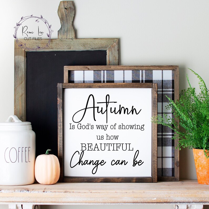 May include: A white wooden sign with the text "Autumn is God's way of showing us how BEAUTIFUL Change can be" in black lettering. The sign is framed with a black and white plaid fabric and a brown wooden frame.