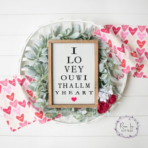 Könnte beinhalten: Ein Holzschild mit weißem Hintergrund und schwarzem Text, der "Ich liebe dich von ganzem Herzen" lautet. Das Schild ist von einem Kranz aus grünen Blättern und einem rosa-weißen Stoff mit Herzen darauf umgeben.