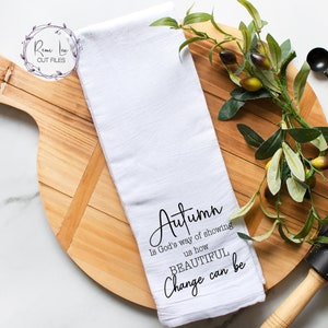 May include: White kitchen towel with black text that reads "Autumn is God's way of showing us how BEAUTIFUL change can be".