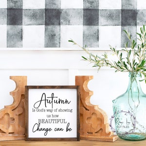 May include: A wooden sign with the text "Autumn is God's way of showing us how BEAUTIFUL Change can be". The sign is sitting on a wooden surface with a vase of greenery and two wooden bookends.