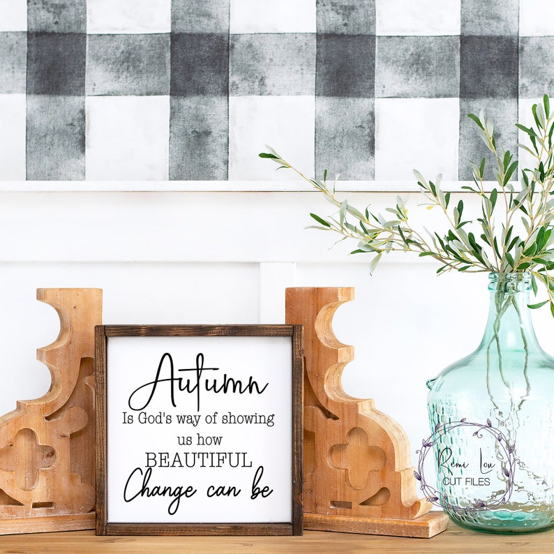 May include: A wooden sign with the text "Autumn is God's way of showing us how BEAUTIFUL Change can be". The sign is sitting on a wooden surface with a vase of greenery and two wooden bookends.