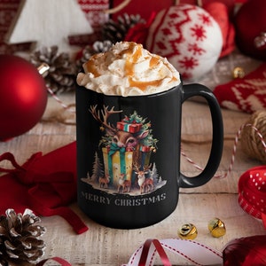 Peut inclure: Mug en céramique noire avec un motif festif représentant un cerf avec des cadeaux et le texte "MERRY CHRISTMAS". La tasse est remplie de crème fouettée et de caramel, parfait pour les fêtes de fin d'année.