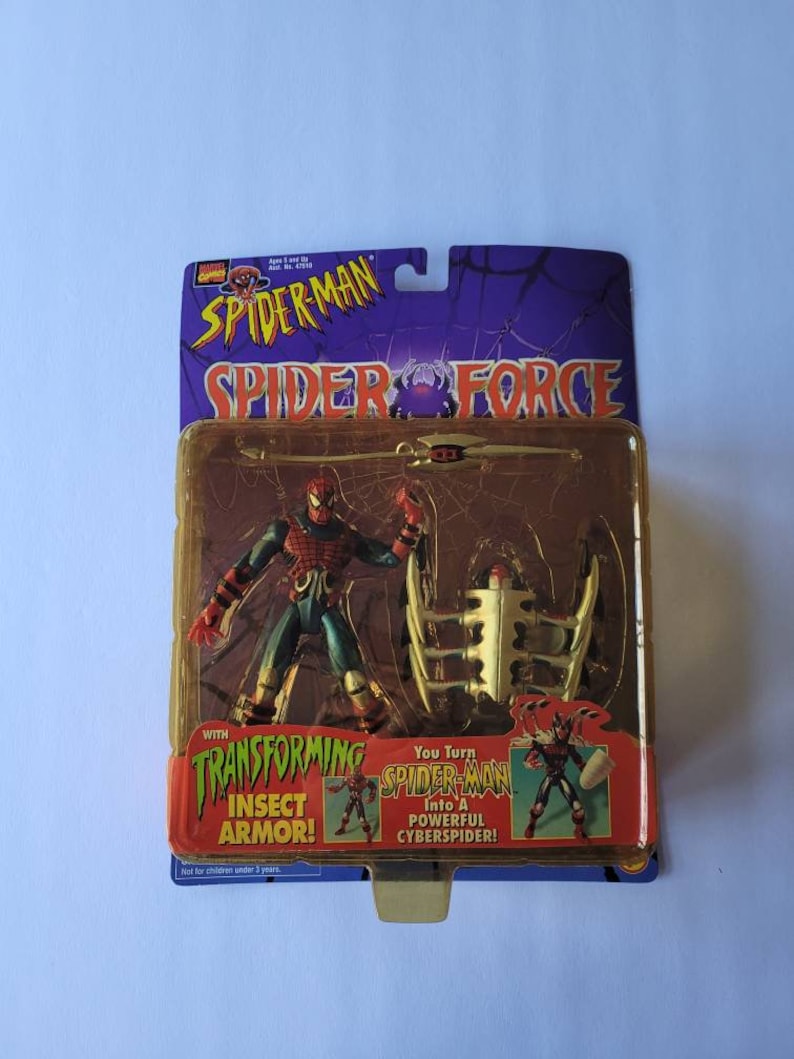 Peut inclure: Une figurine d'action Spider-Man avec une armure d'insecte transformable. La figurine est rouge et bleue avec des toiles d'araign&eacute;e noires et tient une &eacute;p&eacute;e. L'emballage pr&eacute;sente le texte "Spider-Man Spider Force" et "You Turn Spider-Man Into A Powerful CyberSpider!"