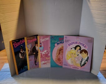 May include: Five vintage Barbie paper doll books with colorful covers. The books feature illustrations of Barbie dolls in various outfits and settings. The books are titled "Barbie Paper Doll" and "Barbie Spring Fashion".