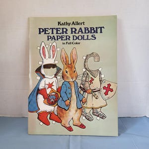 May include: A vintage book titled "Peter Rabbit Paper Dolls in Full Color" by Kathy Alert. The cover features illustrations of Peter Rabbit and other characters as paper dolls, with a light green background.