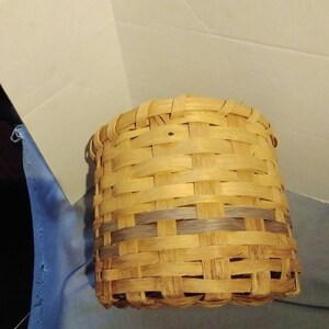 May include: A woven basket made of natural materials, with a light brown color and a darker brown band around the middle.