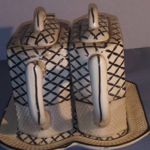 May include: A set of two white ceramic teapots with black and white geometric designs. The teapots have lids and handles and are sitting on a matching tray.