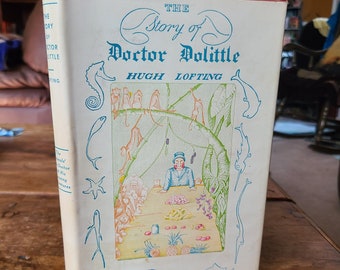 Puede incluir: Un libro antiguo de tapa dura titulado "The Story of Doctor Dolittle" de Hugh Lofting. La portada presenta una ilustración colorida del Doctor Dolittle rodeado de animales, incluidos monos, pájaros y peces.
