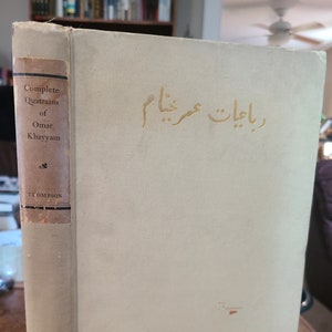 Puede incluir: Un libro vintage titulado "Complete Quatrains of Omar Khayyam" de Thompson. El libro tiene una cubierta blanca con letras doradas y una mancha roja en la parte delantera.