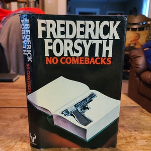 May include: A black paperback book with the title "Frederick Forsyth No Comebacks" on the cover. The cover features a gun tucked inside an open book.