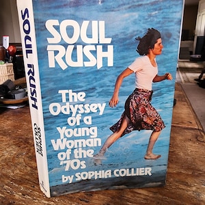 Puede incluir: Un libro titulado "SOUL RUSH" con una portada azul que muestra a una mujer corriendo por el agua. El texto dice "The Odyssey of a Young Woman of the '70s by SOPHIA COLLIER". El lomo también muestra "SOUL RUSH" y "SOPHIA COLLIER".