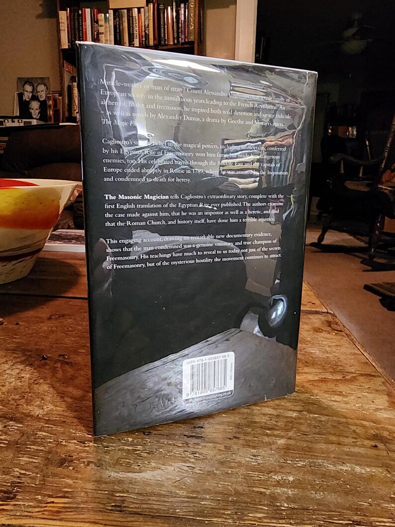 Puede incluir: La contraportada de un libro negro de tapa dura sobre la vida del conde Alessandro Cagliostro, una figura hist&oacute;rica conocida por su participaci&oacute;n en la masoner&iacute;a y la alquimia. El t&iacute;tulo del libro es "El Mago Mas&oacute;nico" y el texto describe la extraordinaria historia de Cagliostro, incluyendo sus viajes por Europa y su eventual condena a muerte por herej&iacute;a en Roma en 1789.