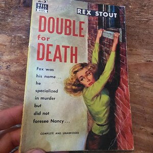 Pode incluir: Um livro de bolso vintage intitulado "Double for Death" de Rex Stout. A capa apresenta uma mulher com uma blusa verde e uma saia castanha, com o título "DOUBLE for DEATH" em letras vermelhas. O livro é um Dell Book, com o preço de 25¢.