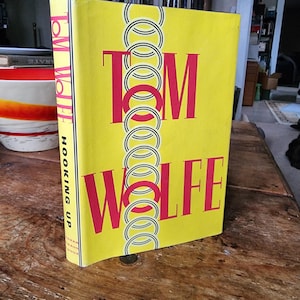 May include: A yellow hardback book with the title "TOM WOLFE HOOKING UP" in black and red lettering. The book cover features a repeating pattern of black and white circles.