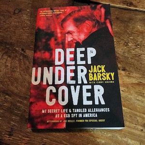 May include: A book titled "Deep Under Cover: My Secret Life & Tangled Allegiances as a KGB Spy in America" by Jack Barsky with Cindy Coloma. The cover features a red and black image of a man's face and the title in white text.