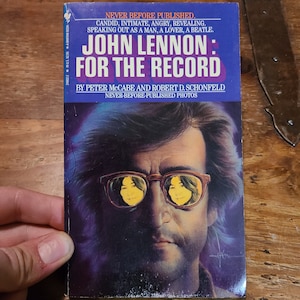 Könnte beinhalten: Ein Buchcover mit einem Foto von John Lennon, der eine Sonnenbrille trägt. Der Titel des Buches lautet "John Lennon: For the Record" und der Untertitel lautet "Nie zuvor veröffentlichte Fotos".