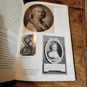 Puede incluir: Un retrato en blanco y negro de una mujer con un cuello de encaje blanco y un vestido negro. El texto debajo del retrato dice "Seraphina Felichiani, Countess de Cagliostro".