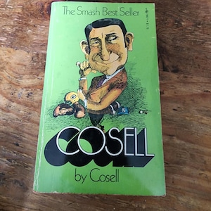 Könnte beinhalten: Ein Vintage-Buch mit dem Titel "COSELL" von Cosell. Das Cover ist grün mit einer Karikatur eines Mannes im Anzug. Der Text "The Smash Best Seller" steht oben. Das Buch liegt auf einer Holzoberfläche.