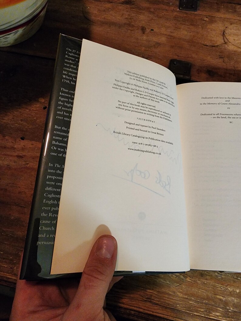 Puede incluir: Un libro blanco con texto negro en la portada. El libro est&aacute; abierto en una p&aacute;gina con una dedicatoria e informaci&oacute;n de copyright. El texto en la p&aacute;gina dice: "Dedicado con amor a la Orden Mas&oacute;nica, a la memoria del Conde Alessandro..." y "Dedicado a todos los masones que fueron... en la tierra, el mar o... BC."