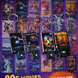 May include: Collection of 80s movie VHS keychain replicas. Keychains feature iconic films like "E.T.", "Back to the Future", and "The Goonies". Each keychain has a metal ring and chain. The background displays various VHS movie covers.