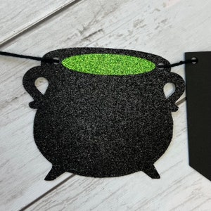 Puede incluir: Caldero negro con purpurina verde en su interior, parte de una pancarta de Halloween.