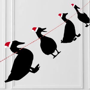 May include: A string of black goose silhouettes wearing red and white Santa hats, strung on a red and white twine. The geese are in various poses, creating a festive holiday decoration.