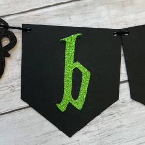 Puede incluir: Pancarta negra con una letra "b" de purpurina verde en una fuente g&oacute;tica.