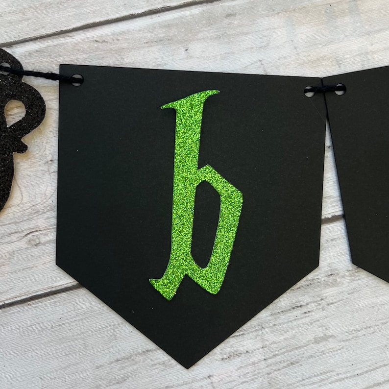 Puede incluir: Pancarta negra con una letra "b" de purpurina verde en una fuente g&oacute;tica.