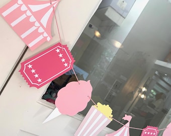 May include: Pink and white paper garland with a circus theme. The garland includes a tent, ticket, cotton candy, popcorn, and stars.