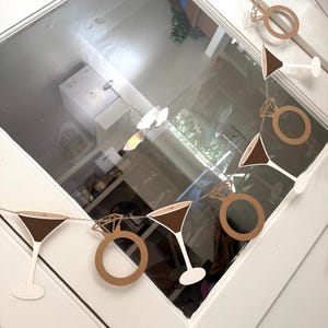 May include: A garland featuring cut-out shapes of martini glasses and diamond rings. The martini glasses have brown tops and white stems. The diamond rings are brown. The garland is strung on a thin string, perfect for a bridal shower or engagement party.