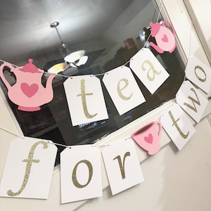 May include: A pink and gold tea party banner with the words "tea for two" and images of teapots and teacups.