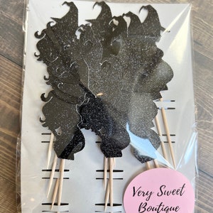 Puede incluir: Un paquete de adornos para cupcakes con silueta de bruja negra con purpurina y palitos de madera. El paquete tiene una pegatina circular rosa con el texto "Very Sweet Boutique creaciones hechas a mano".