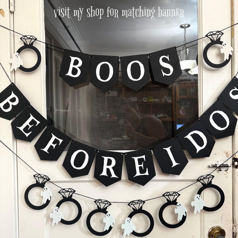May include: Black banner with white text spelling "BOOS BEFORE I DO" and diamond ring and ghost decorations. The banner is strung across a doorway, perfect for a Halloween or spooky wedding theme.