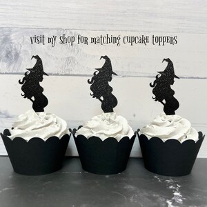 Puede incluir: Tres envoltorios de cupcake negros con glaseado blanco y adornos de cupcake de bruja con purpurina negra. Los adornos son siluetas de brujas embarazadas con escobas. El texto "visit my shop for matching cupcake toppers" est&aacute; en la parte superior de la imagen.