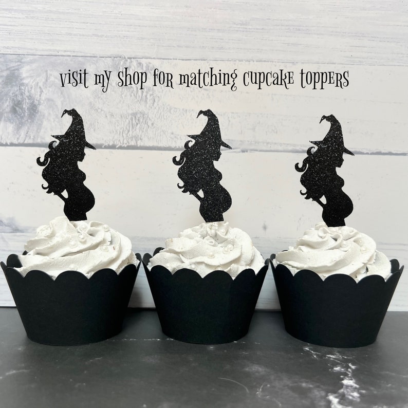 Puede incluir: Tres envoltorios de cupcake negros con glaseado blanco y adornos de cupcake de bruja con purpurina negra. Los adornos son siluetas de brujas embarazadas con escobas. El texto "visit my shop for matching cupcake toppers" est&aacute; en la parte superior de la imagen.