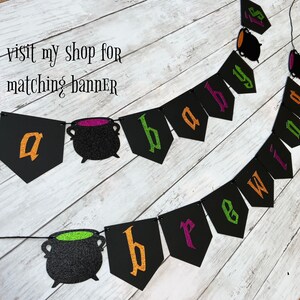 Puede incluir: Una pancarta de baby shower de Halloween negra y verde con las palabras "a baby is brewing" y decoraciones de caldero.