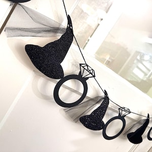 May include: A black glitter witch hat and diamond ring banner. The banner is strung on a black string and includes black tulle. The witch hats are covered in black glitter. The diamond rings are black cutouts.