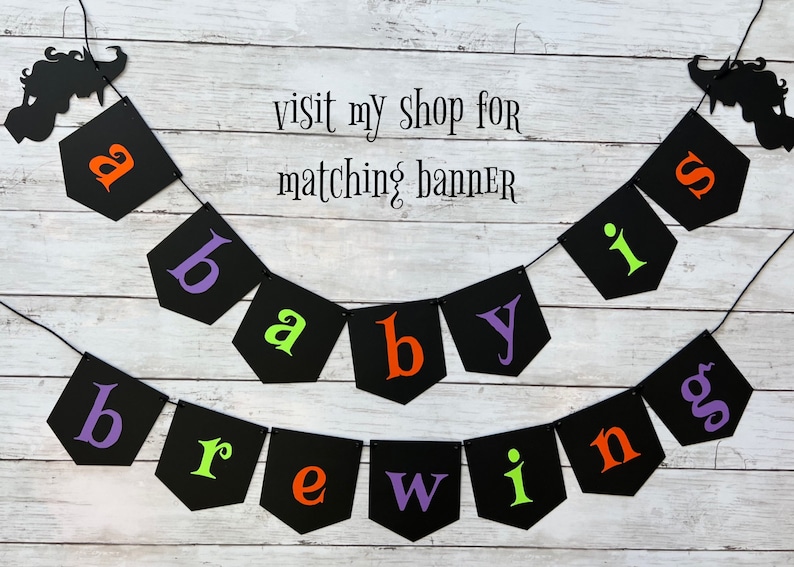 Puede incluir: Una pancarta de baby shower de Halloween en blanco y negro con el texto "a baby is brewing". La pancarta est&aacute; hecha de cartulina negra con letras blancas y tiene una silueta de bruja y un fantasma en cada extremo.