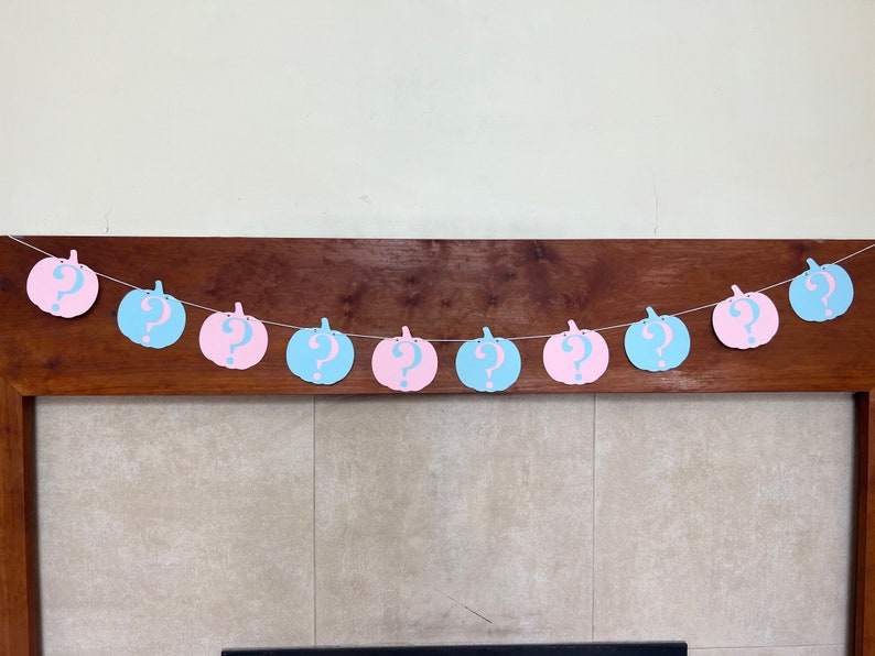 May include: A gender reveal banner with alternating blue and pink pumpkins with question marks on them.