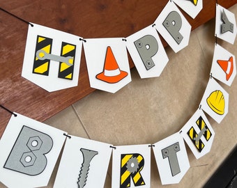 May include: A white construction-themed banner with the words "Happy Birthday" in black letters. Each letter has a different construction-themed image, such as a wrench, a screw, a saw, and a hard hat.