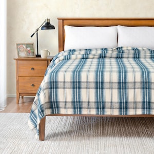 Peut inclure: Une couverture en plaid bleu et blanc sur un cadre de lit en bois avec des oreillers blancs. La couverture a une texture douce et duveteuse.